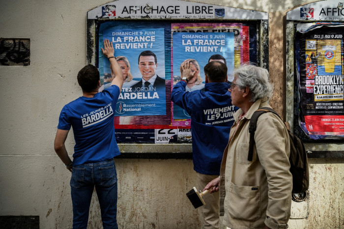 Rassemblement National (RN) party volunteers paste campaign posters