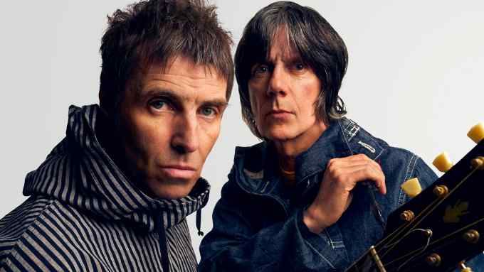 Liam Gallagher, wearing a striped hoodie and holding a guitar, and John Squire, wearing a denim jacket, look moodily at the camera