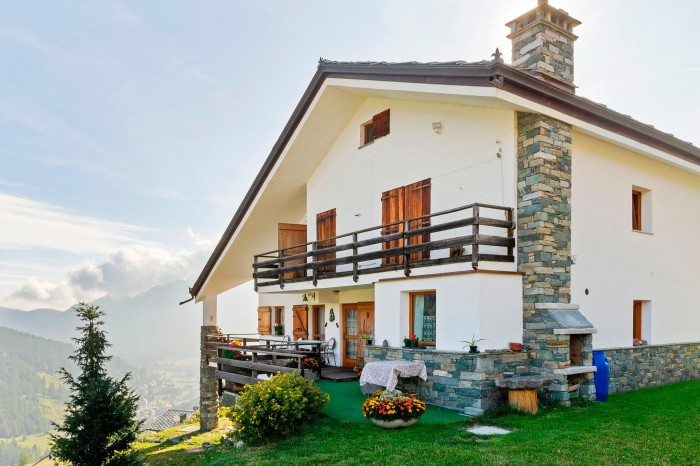 villa exterior with green lawn, balcony, mountains in the distance