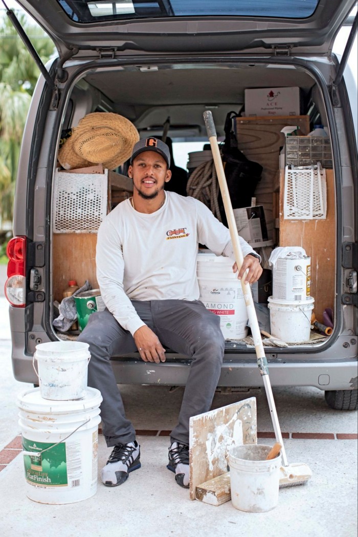 A man in working  clothes sitting behind the storage area of a van filled with his tools