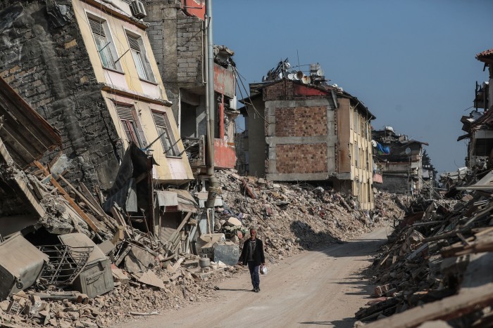 A man walks past collapsed buildings in the aftermath of powerful earthquakes in Hatay, Turkey
