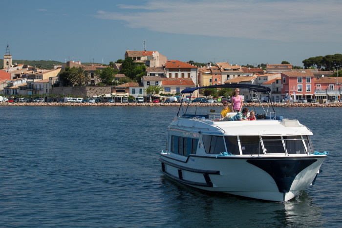 Scenic view of a leisure boat sailing close to shore in front of an old European town featuring traditional architecture and a lively waterfront promenade