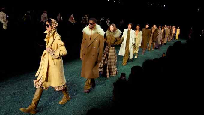 Models in coats, boots and headscarves walk in a line on fake grass