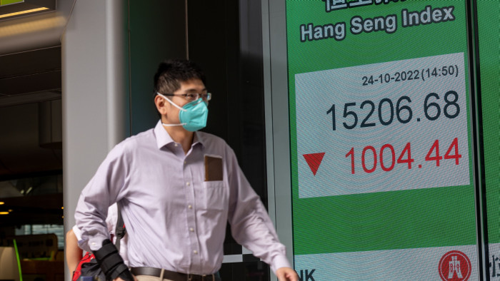 A man walks past an electronic billboard displaying the Hang Seng index