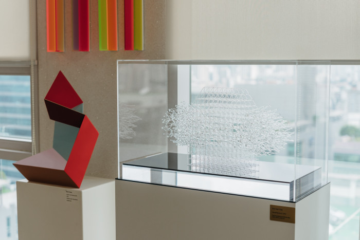 Two sculptures sit on plinths: a red metal geometric shape, and a rectangular perspex piece containing an intricate pattern