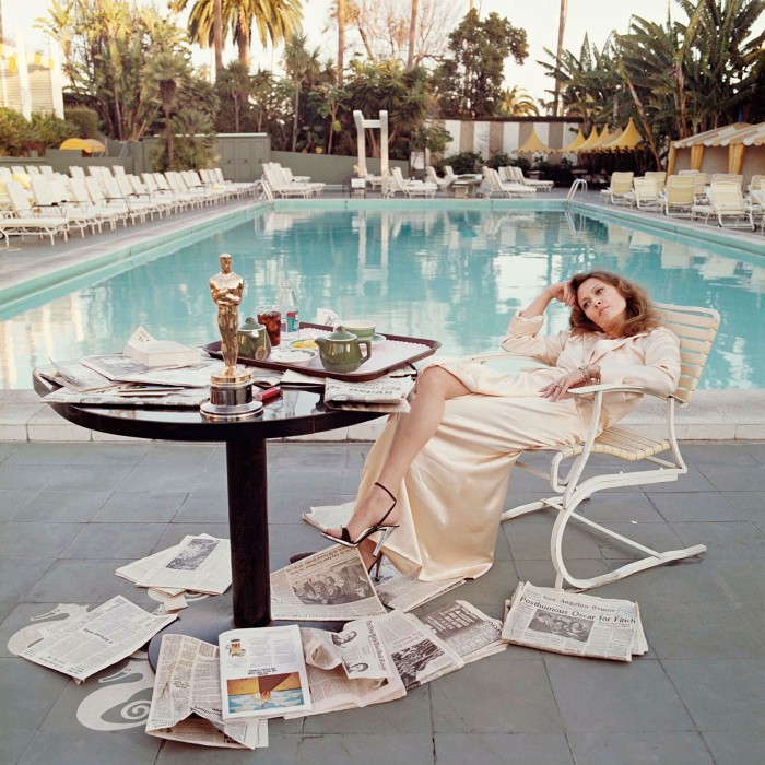 woman lounging in chair by pool surrounded by newspapers on the ground and on table