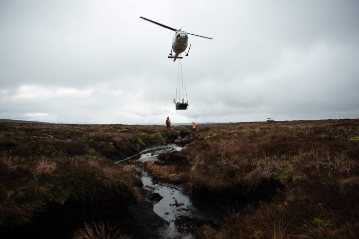 A helicopter hovers above a peatland restoration project in Cumbria, northern England