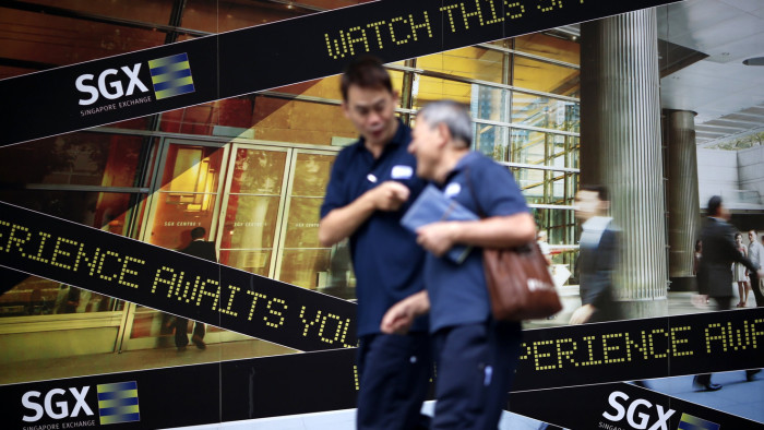 People walk past a logo of the Singapore Stock Exchange