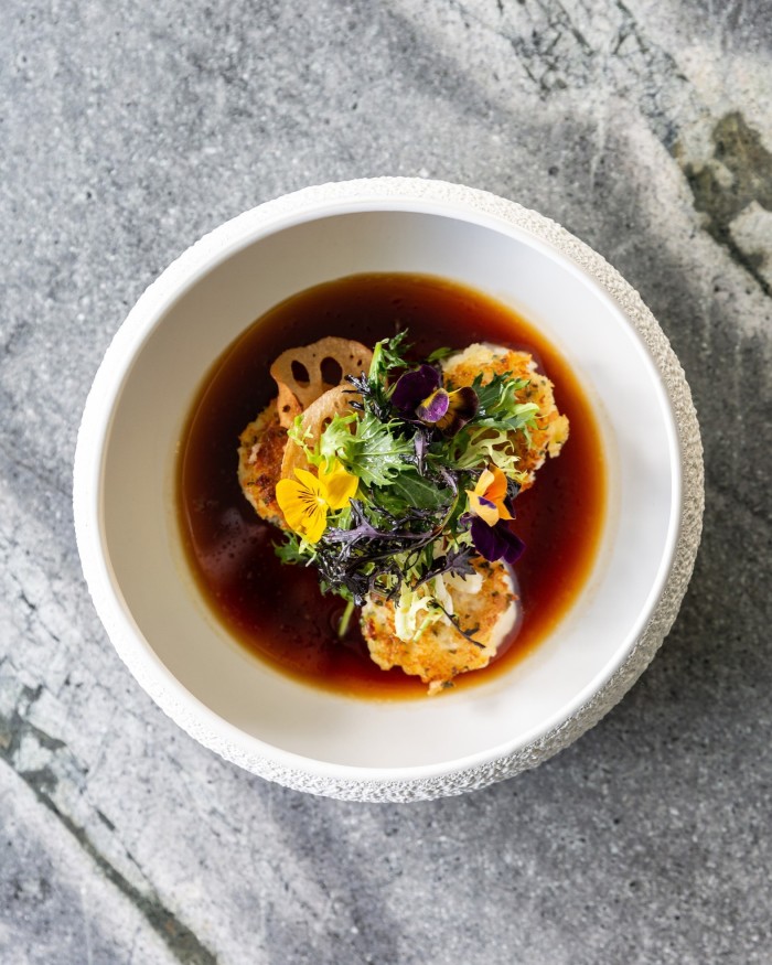 A bowl of brown broth with dumplings topped with edible flowers at the Royal Copenhagen’s Issei restaurant