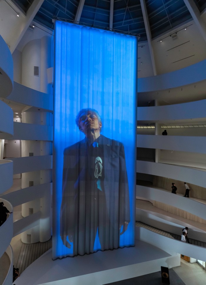 A six-storey-high piece of fabric hangs in a circular atrium with a man in a suit projected on to it