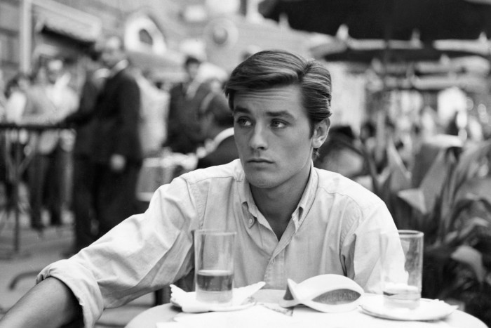 A dark haired young man sits at a cafe table