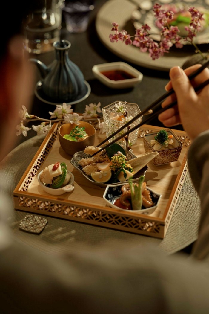 Someone using chopsticks to pick up food from a variety of small dishes on a square platter