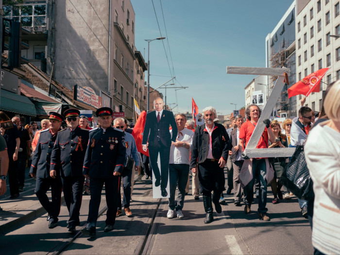 Men in military uniforms and some in civilian clothes march down a street bearing a lifesize cutout of the Russian President 