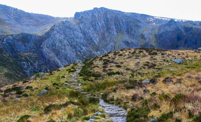 A path across moorland on Cwm Idwal, behind which is a rocky hill