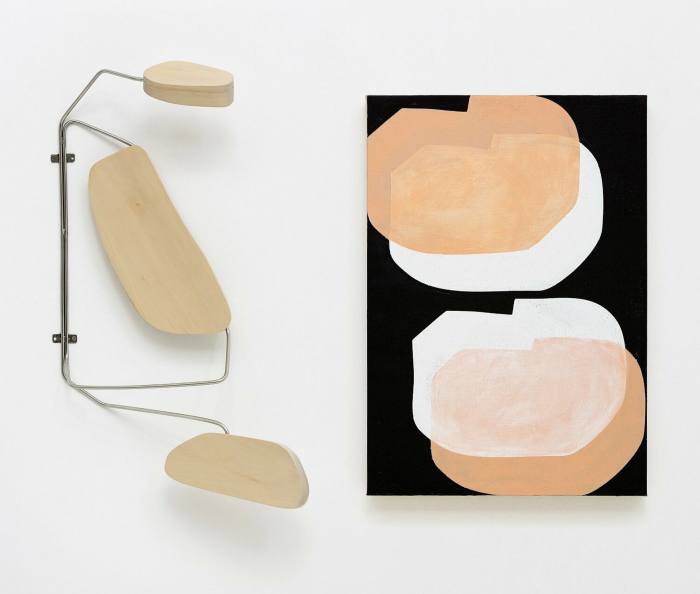 A wall-mounted sculpture which looks like a desk lamp made of wood and a print with floating white and peach circles on a black background
