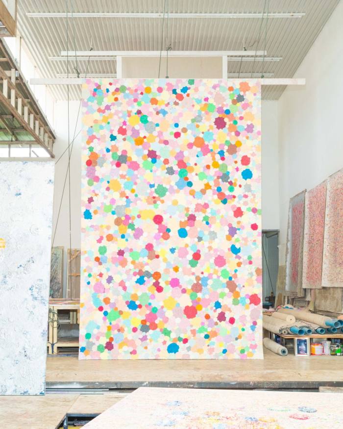 A large art work covered in colourful dots hangs like a scroll from a studio ceiling