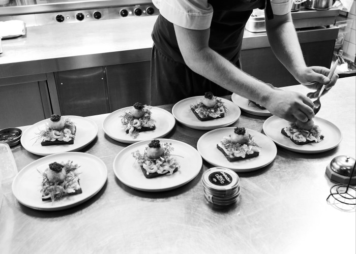 A chef preparing several plates of shrimp on toast with fried egg and caviar at Palægade