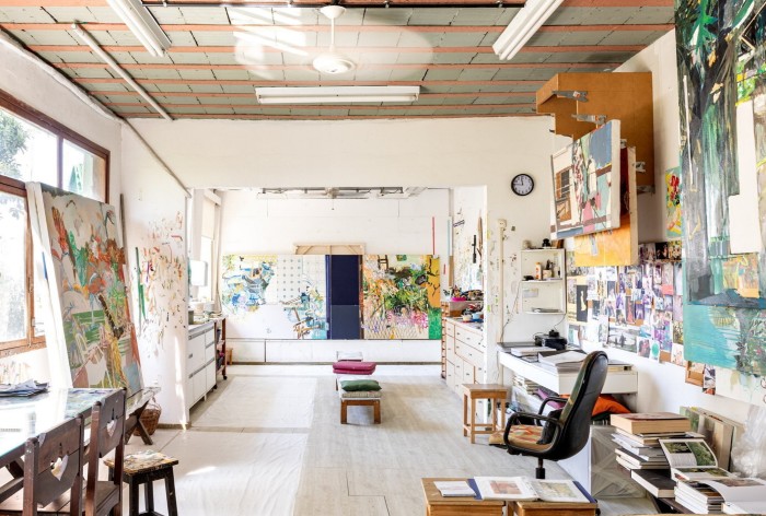 A brightly lit studio with furniture, canvases and other pictures pinned to one wall