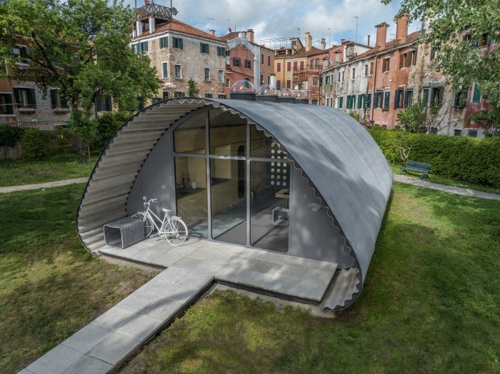 A grey concrete shelter with an arched roof and glass doors, with a bike parked in front