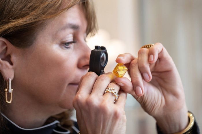 woman inspecting a rough yellow diamond using a jeweler’s loupe