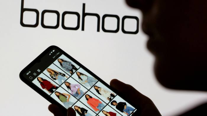 A woman with the Boohoo website on a mobile phone and the company’s logo in the background