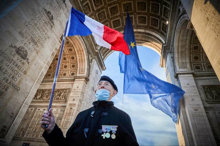 A French veteran holds a tricolore next to the EU flag at the Arc de Triomphe. France currently holds the EU presidency