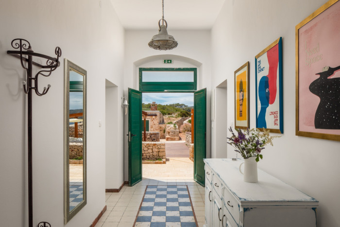 A hallway with white walls, tiled floor and framed posters looks out on to a sunny courtyard