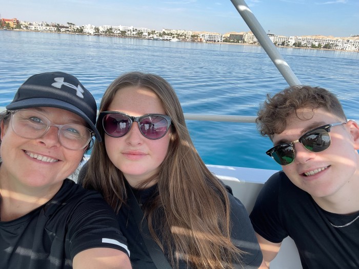 A middle-aged woman and a teenage boy and girl pose for a selfie on a boat