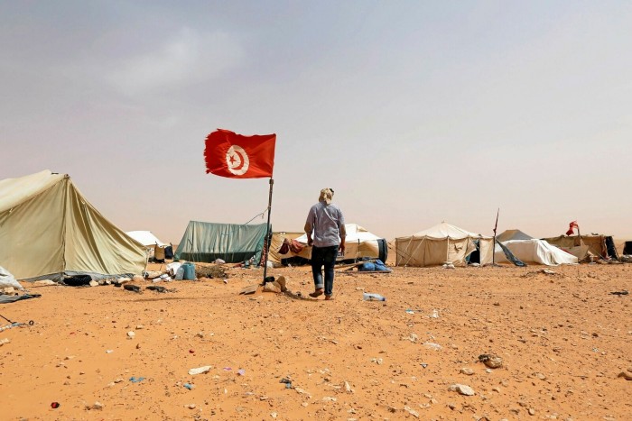 A man stands by a Tunisian flag in front of tents in the desert, where a sit-in against the Kamour production plant took place