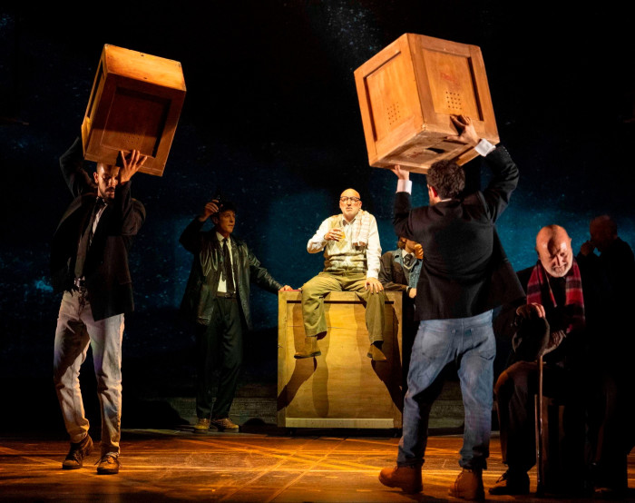 Workmen carry crates across a darkened stage