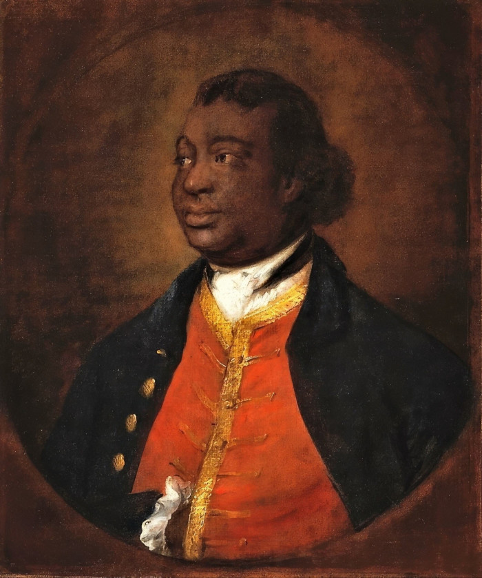 A Black man, smiling gently, looking to one side, stands with one hand tucked into his gold-braided red waistcoat