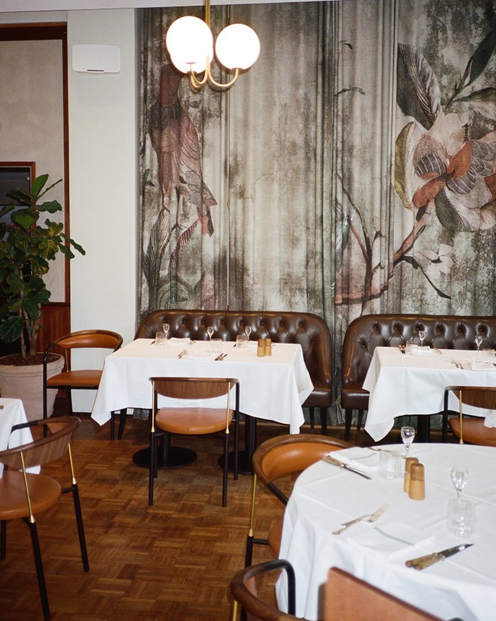 Møntergade’s dining space with brown-leather seating, globe pendant lamps and curtains covered in large illustrations of tropical birds and plants