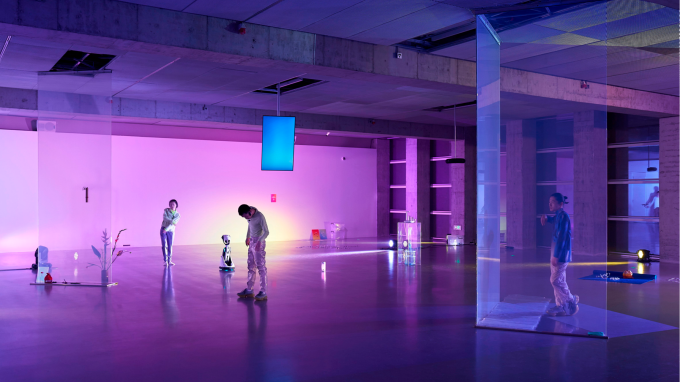 People looking at small sculptures in a purple-lit gallery