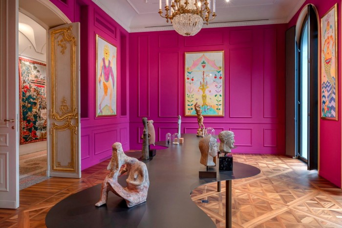 The vivid pink walls of a room in the Fondazione Luigi Rovati, hung with contemporary paintings. On a long curvy dark-wood table in the middle of the room sit Etruscan artefacts