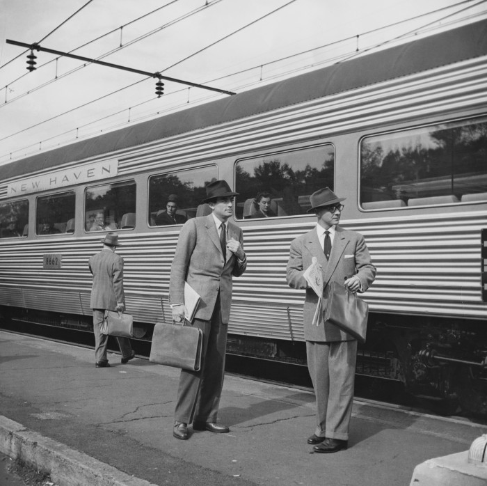 Gregory Peck holding a briefcase and standing on a platform in front of a commuter train with a co-actor in the 1956 film The Man in the Gray Flannel Suit