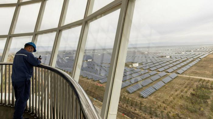 A worker stands in an observation tower over looking photovoltaic panels at a solar farm operated by Yellow River Power in China