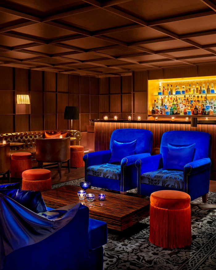 Neon-blue armchairs and a leather sofa in front of the bar in the hotel’s Punch Room