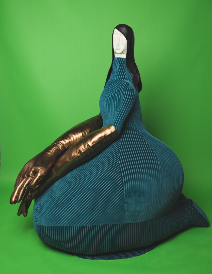 Large sculpture made out of teal corduroy of a woman sitting on her knees with large bronze gloves
