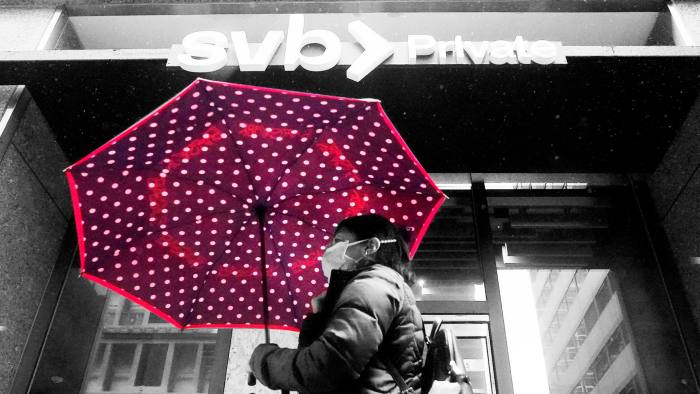 A woman holding an open umbrella walks past a SVB branch