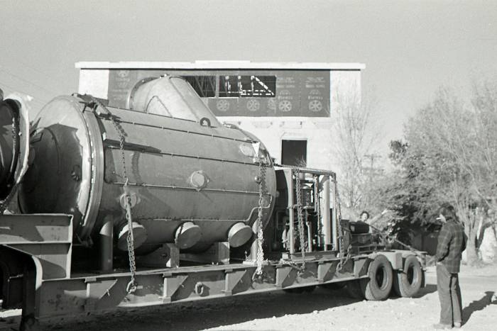 Black and white photo of a large cylindrical machine arriving on a flatbed truck