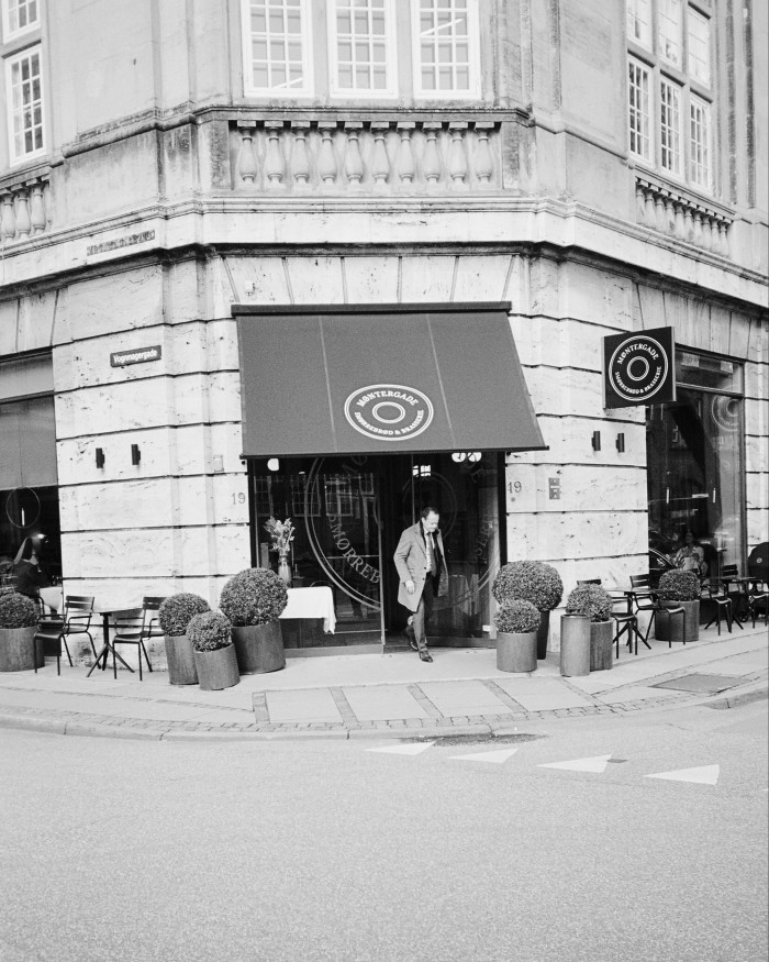 A black and white image of the entrance to Møntergade, with a man in a raincoat leaving the restaurant