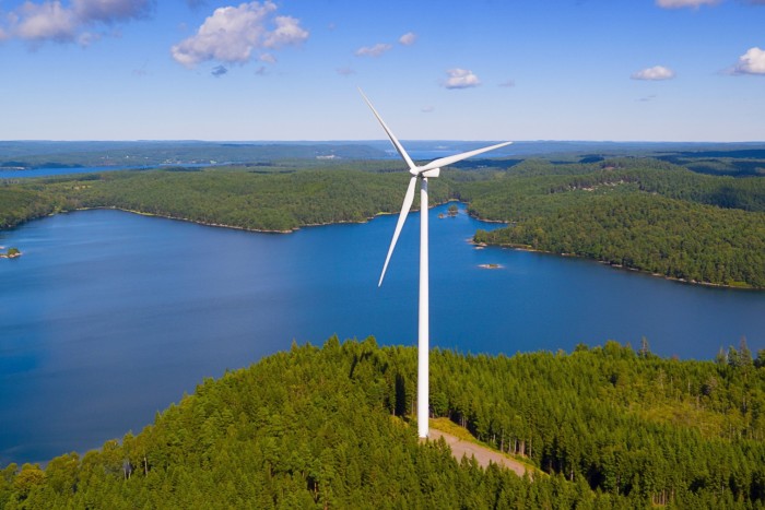 A wind turbine amid forested land and lake
