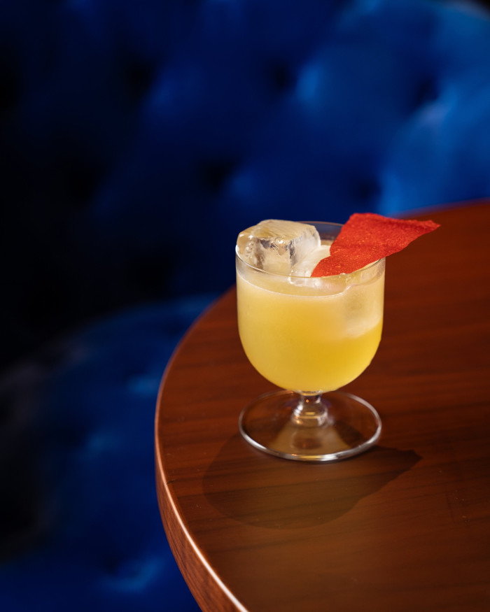 The Red Dot: a yellow cocktail in a small glass with an ice cube and triangular red wafer on its surface, in the hotel’s Punch Room bar 