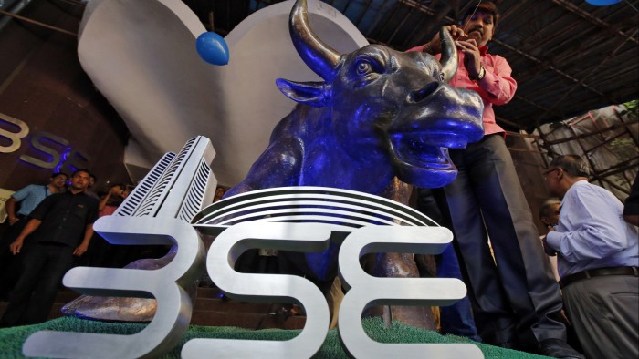 A man ties a balloon to the horns of a bull statue at the entrance of the Bombay Stock Exchange