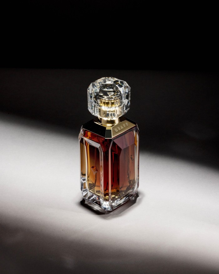 A luxurious glass perfume bottle with a rich amber-colored liquid, featuring a large, multifaceted clear crystal cap and gold accents