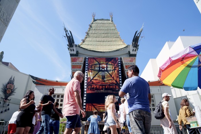 People walking by a Chinese theatre which has a huge film poster on display