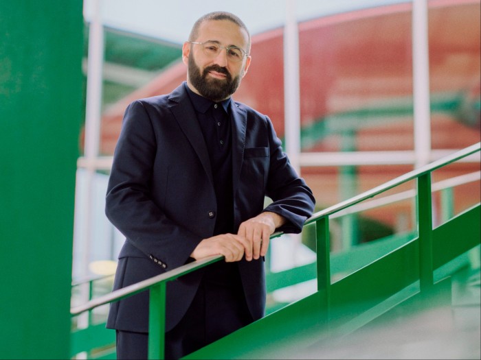 A man in a dark suit stands gently smiling by a green metal railing