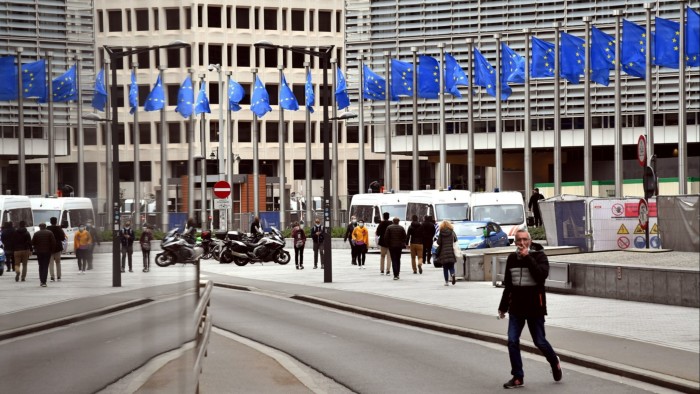 Pedestrians pass EU flags flying outside the headquarters of the European Commission, in Brussels