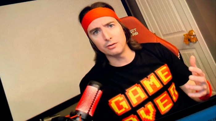 A man wears an orange bandana around his head and a T-shirt with the slogan ‘Game Over’
