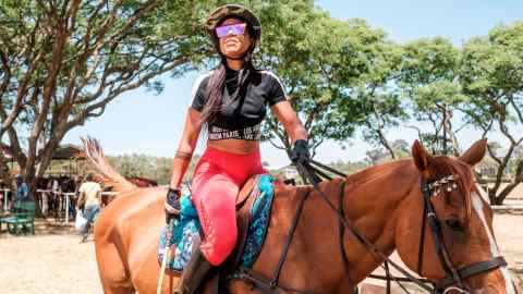 A woman sits astride a horse in full polo kit of helmet, gloves, sunglasses and mallet